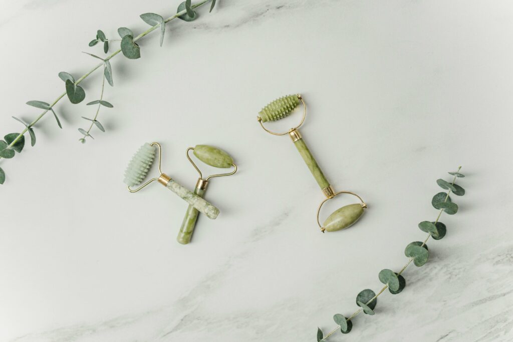 Elegant jade facial rollers and eucalyptus leaves on marble surface, promoting a spa-like ambiance.